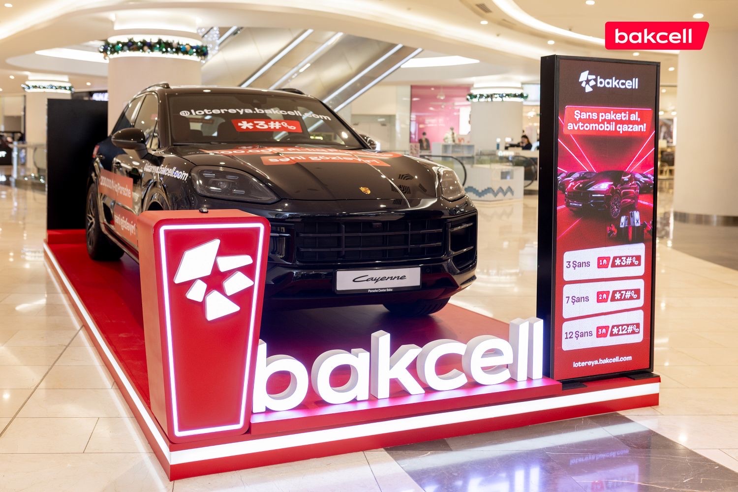 Bakcell uduş lotereyasının Bakıda yerləşən ticarət mərkəzində BTL aktivasiyası, brend podium üzərində Porsche Cayenne əsas mükafatı və *3#, *7#, *12# şans paketlərini tanıdan totem